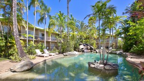 Una piscina circondata da palme e rocce, con un edificio sullo sfondo.