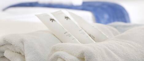 A neatly folded white towel with a tag on it, placed on a bed with a blue and white striped blanket.