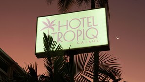 Segnale per 'Hotel Tropiq Cairns' con palme sullo sfondo.