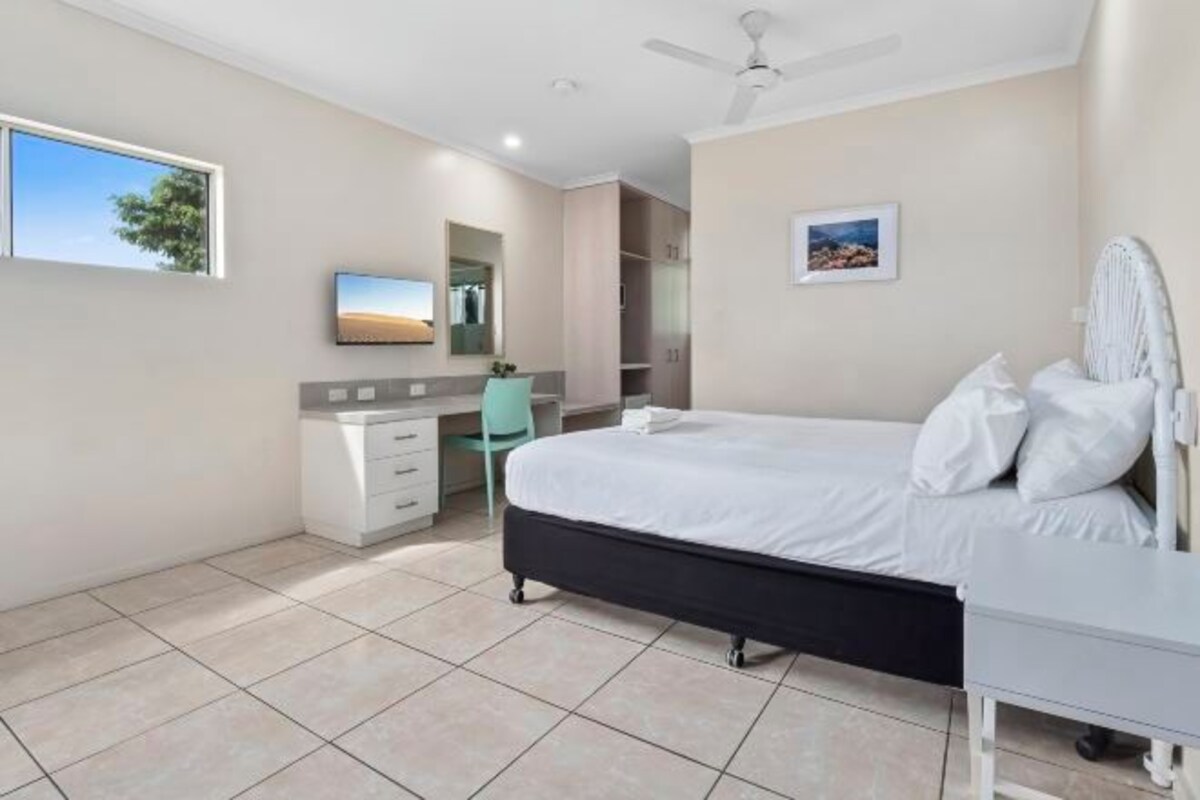 A bedroom with a bed, a desk, a chair, a ceiling fan, and a window.