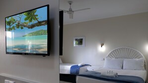 Una camera d'albergo con un letto, una ventola a soffitto, una TV fissata al muro e un piccolo quadro appeso alla parete.
