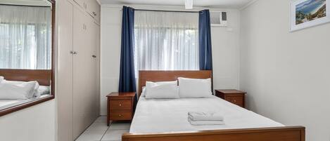 Habitación de hotel con cama, mesita de noche y ventilador de techo, además de ventana con cortinas.