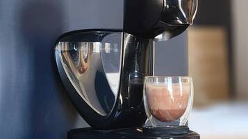 A coffee machine with a cup of coffee, a plate of macarons, and a coffee grinder on a countertop.