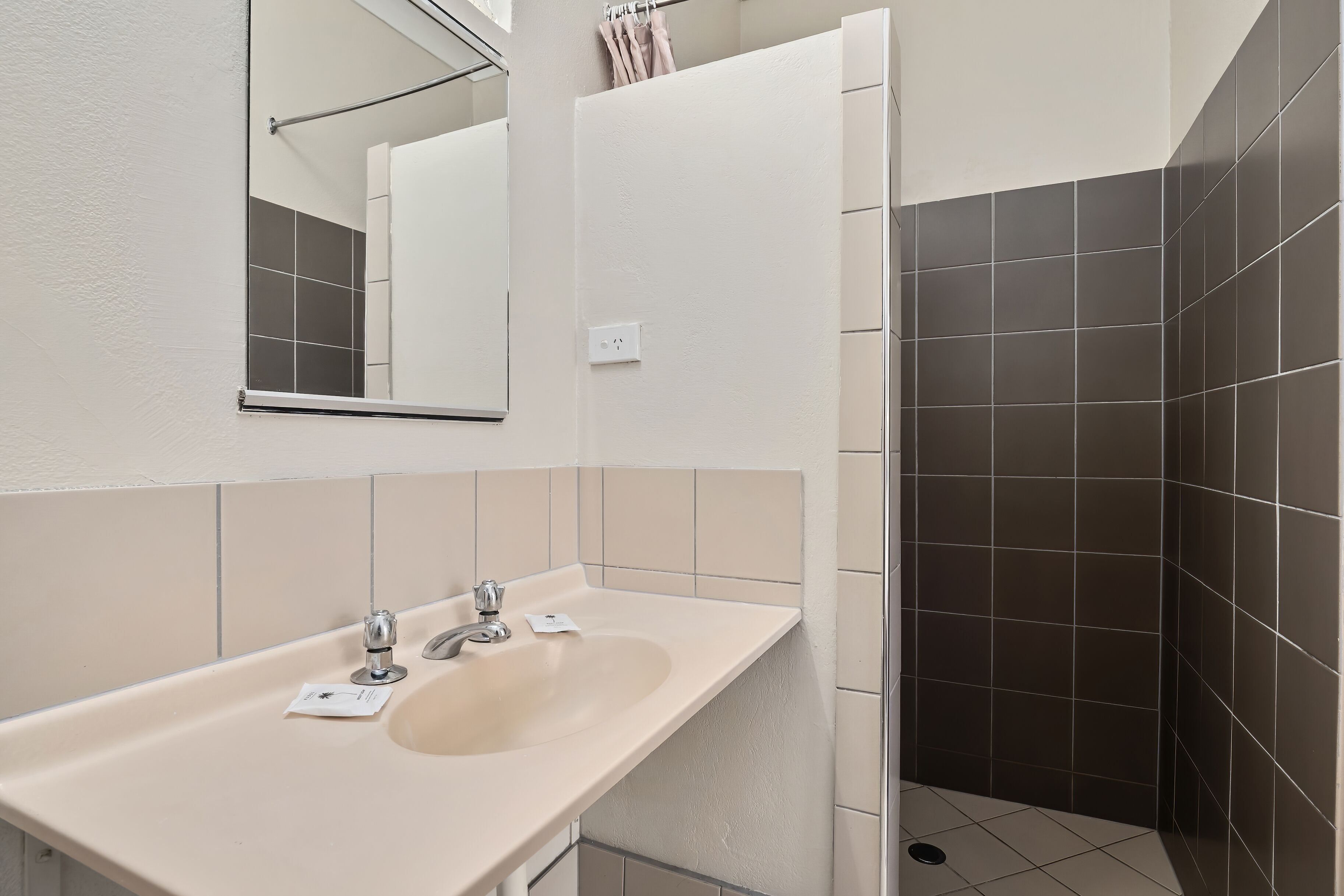 A modern bathroom with a beige sink, a mirror, and dark tiled walls.
