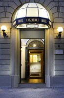 The entrance to Hotel Calzaiuli with a sign above the door and a lamp on either side.