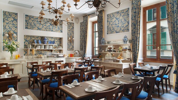 A dining area with multiple tables and chairs, a chandelier, and patterned wallpaper. - FH55 Hotel Calzaiuoli (Florence)