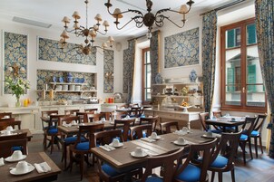 A dining area with multiple tables and chairs, a chandelier, and patterned wallpaper.