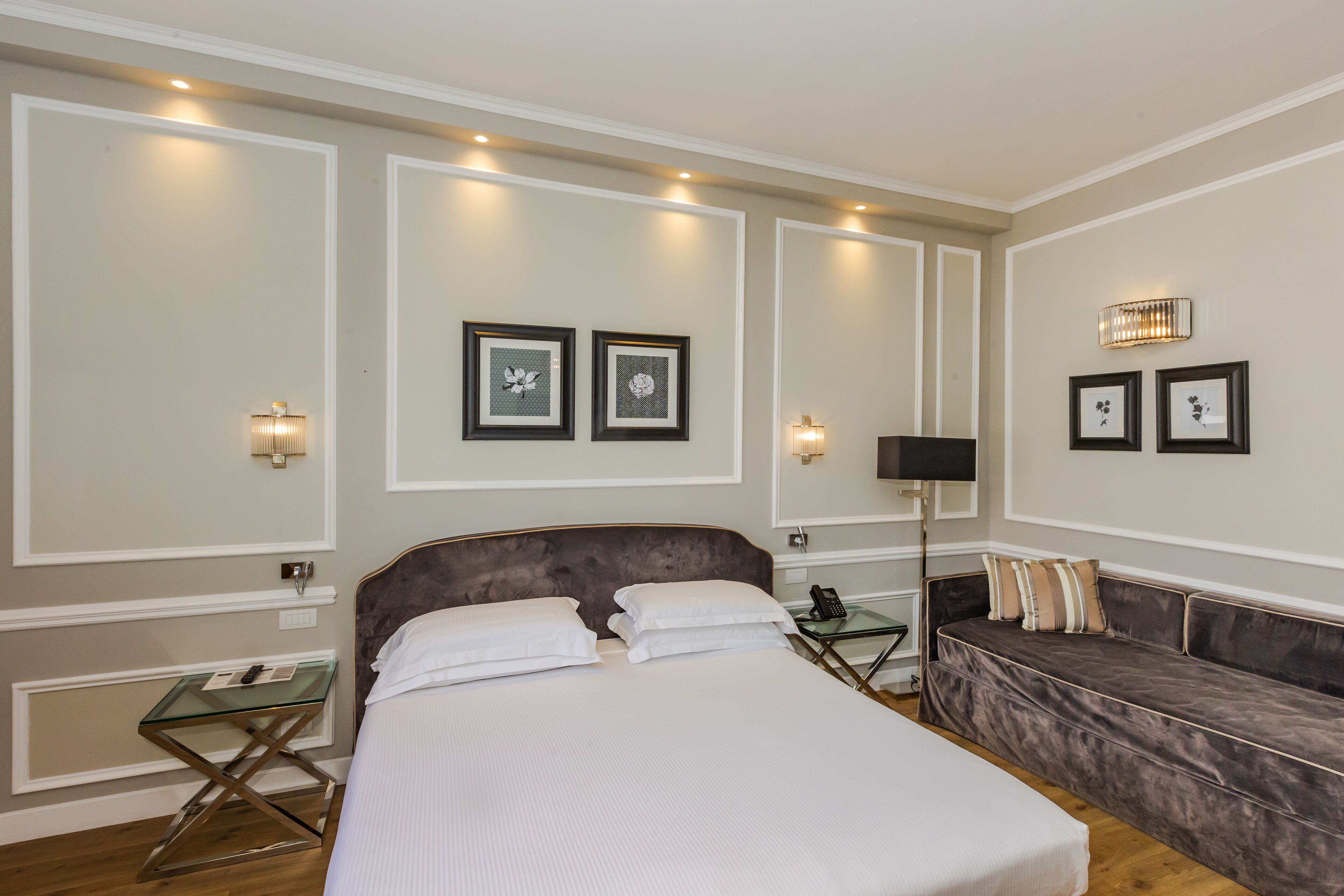 Una camera d'albergo con un letto grande, un divano, un tavolino in vetro e quadri appesi alle pareti.