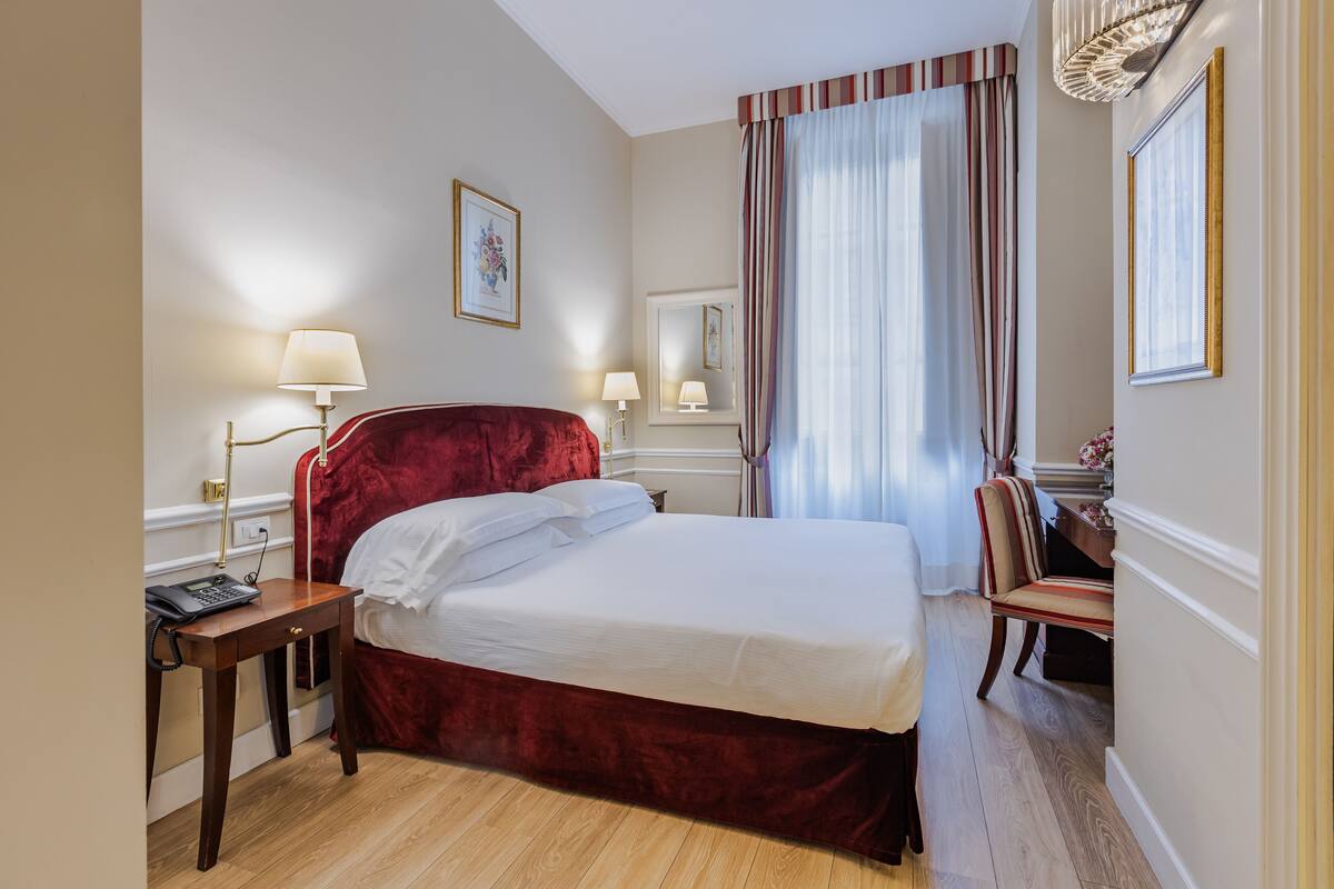 Ein Hotelzimmer mit einem großen Bett, Nachttischlampen, einem Schreibtisch mit Telefon und einem Sessel.