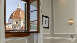 A room with a window view of a historic building, a framed picture on the wall, and a wall-mounted light fixture. - FH55 Hotel Calzaiuoli (Florence)