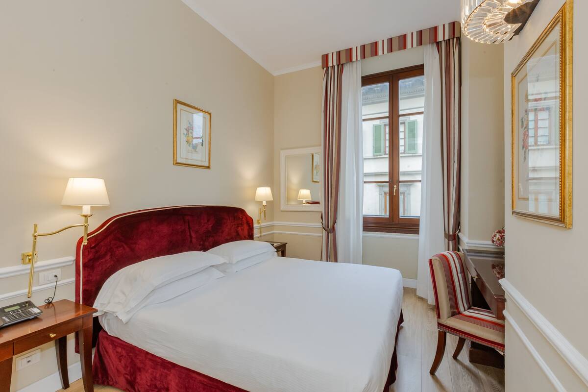 Ein Hotelzimmer mit einem großen Bett, Nachttischlampen, einem Sessel, einem Schreibtisch und einem Fenster mit Vorhängen.