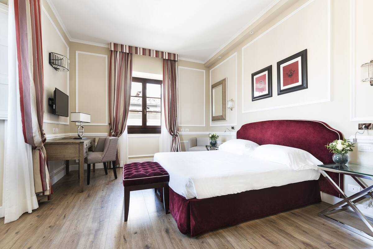 Ein Hotelzimmer mit einem großen Bett, einem Schreibtisch, einem Sessel und einem Fernseher.