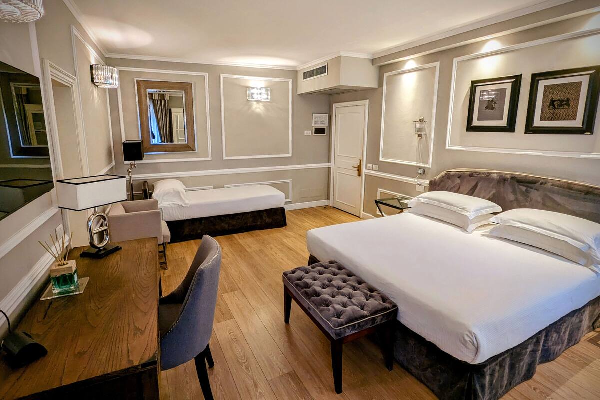 Ein Hotelzimmer mit zwei Einzelbetten, einem großen Bett, einem Schreibtisch mit Stuhl, einem kleinen Tisch und einem Spiegel.