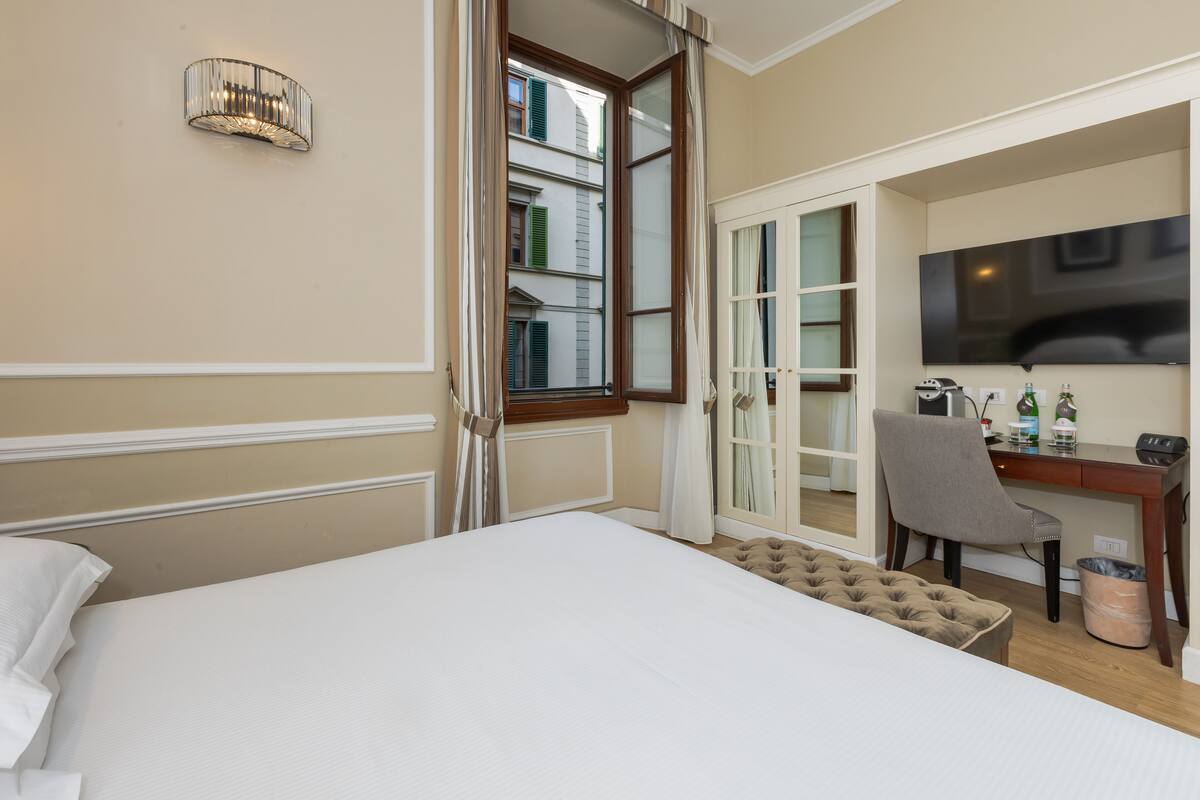 Ein Hotelzimmer mit Bett, Schreibtisch mit Stuhl, Fernseher und einem Fenster mit Vorhängen.