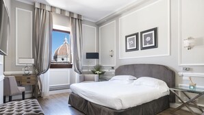 A hotel room with a large bed, a desk, a chair, and a view of a dome structure.
