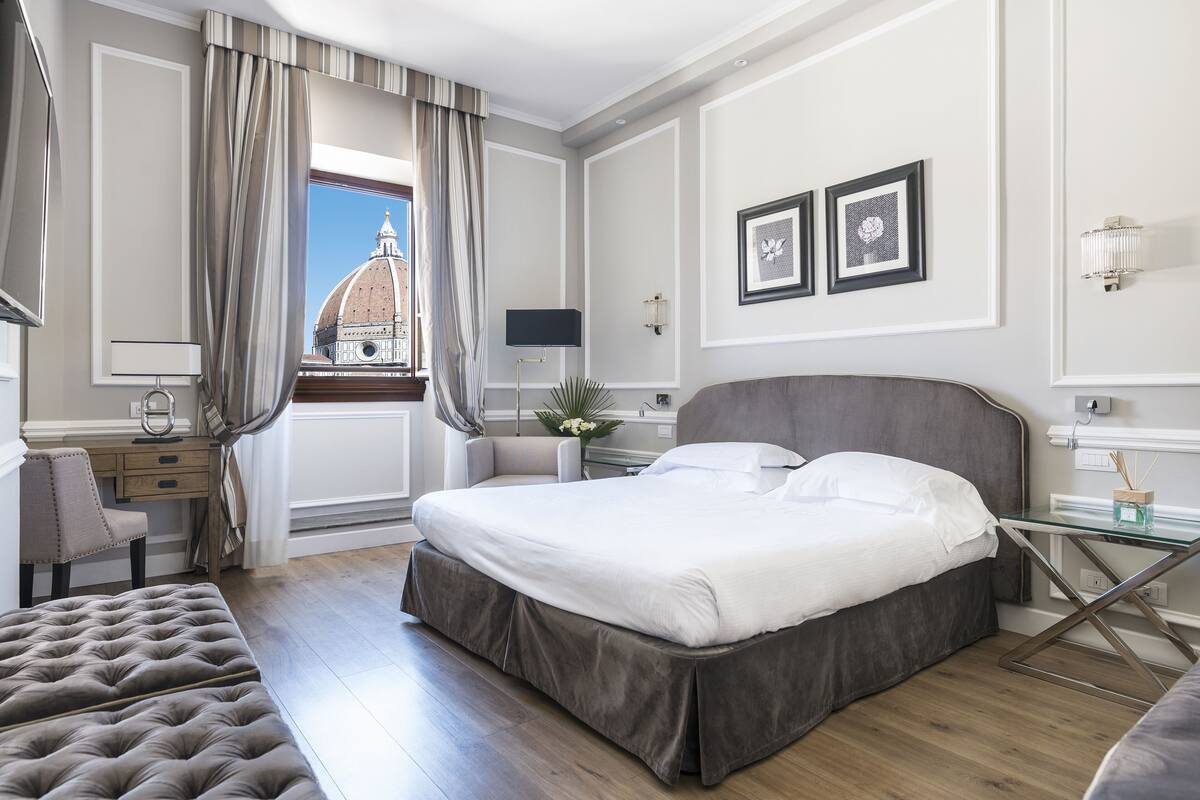 Ein Hotelzimmer mit einem großen Bett, einem Schreibtisch, einem Stuhl und Blick auf eine Kuppelstruktur.