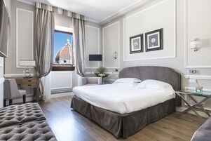 A hotel room with a large bed, a desk, a chair, and a view of a dome structure.