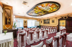 A banquet hall with rows of tables, a stained glass ceiling, and a large painting on the wall.