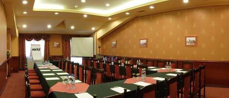 Una sala de conferencias con largas mesas, sillas y una pantalla para proyector.
