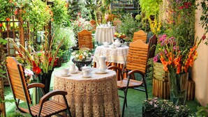 A round table with a lace tablecloth, surrounded by wooden chairs, in a garden setting with various plants and flowers. - Hotel Europejski (Kraków)