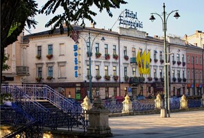 Un hotel con fachada clásica europea, varios balcones con jardineras florales y un llamativo letrero amarillo.