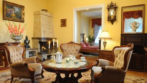 A traditional room with a fireplace, four armchairs, a round table with tea set, and classic decor. - Hotel Europejski (Kraków)