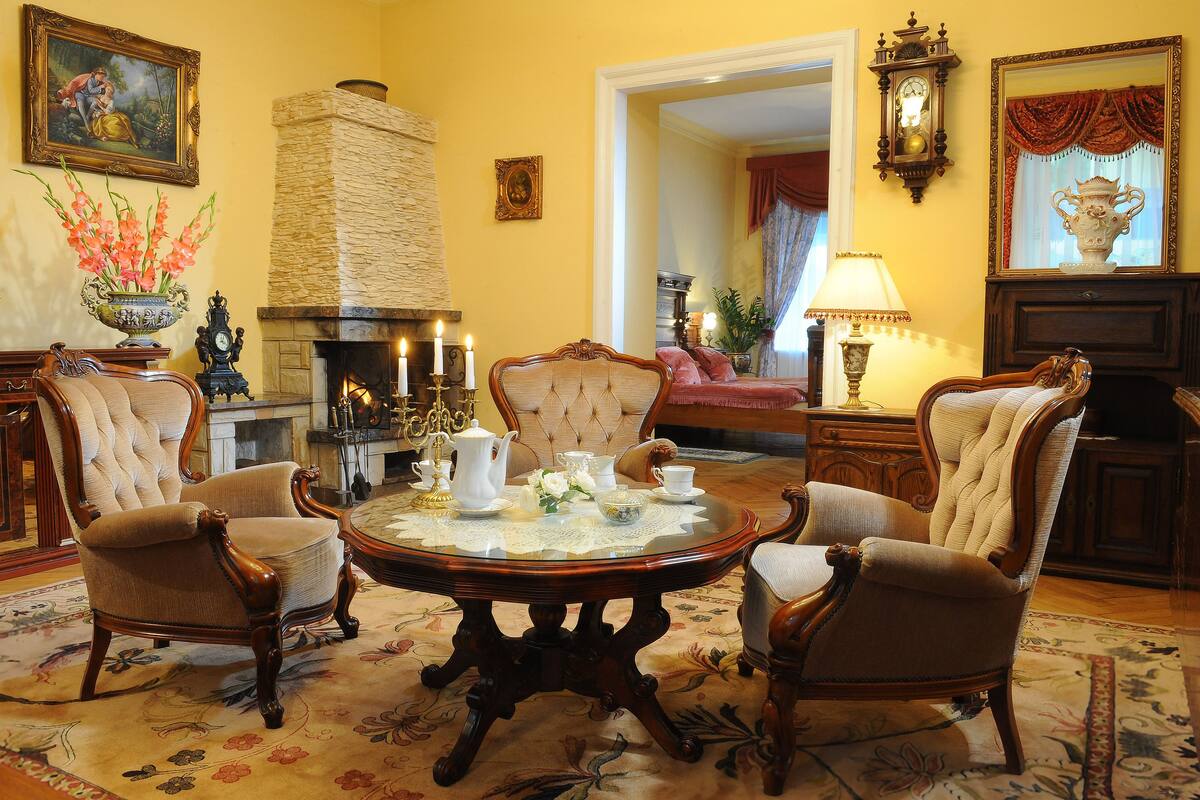 A traditional room with a fireplace, four armchairs, a round table with tea set, and classic decor.