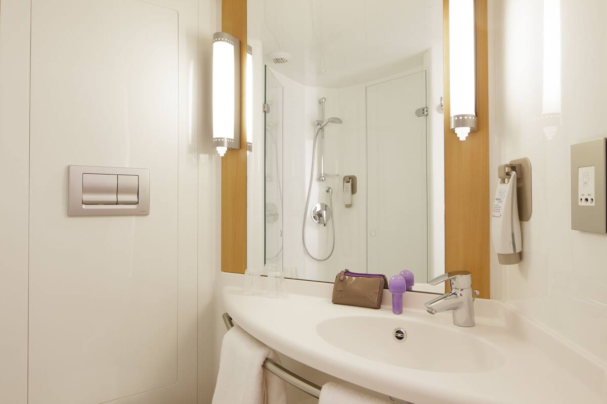 A modern bathroom with a white sink, a mirror, a shower, and a towel rack.