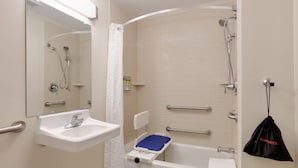 Un baño con lavamanos, espejo, ducha y barras de apoyo.