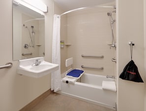 Un baño con lavamanos, espejo, ducha y barras de apoyo.