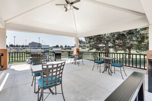 An outdoor patio with tables and chairs, a ceiling fan, and a view of a parking lot and trees.