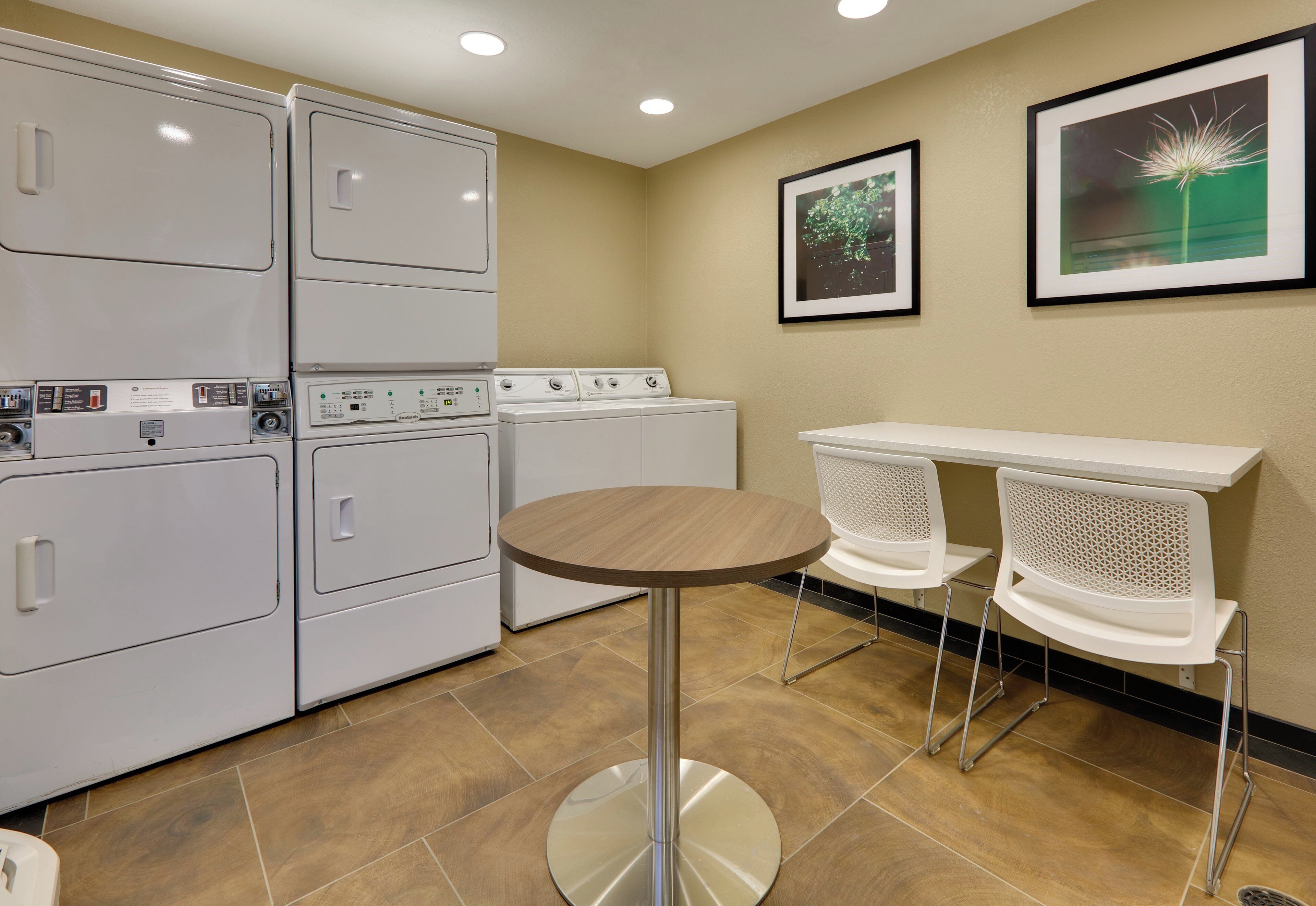 A laundry room with stacked washers and dryers, a round table, and two chairs.