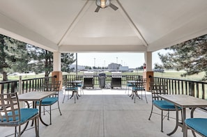 Un patio exterior con mesas y sillas, una parrilla y vistas a un estacionamiento y edificios a la distancia.