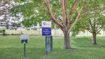 A pet-friendly area sign with a paw print logo, a sign for a pet waste station, and a large tree in the background.