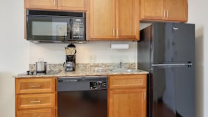 Una cocina compacta con armarios de madera, microondas, cafetera, lavavajillas y refrigerador.