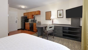 Una habitación de hotel con cama, escritorio, silla, kitchenette y televisor.