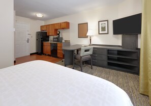 Una habitación de hotel con cama, escritorio, silla, kitchenette y televisor.