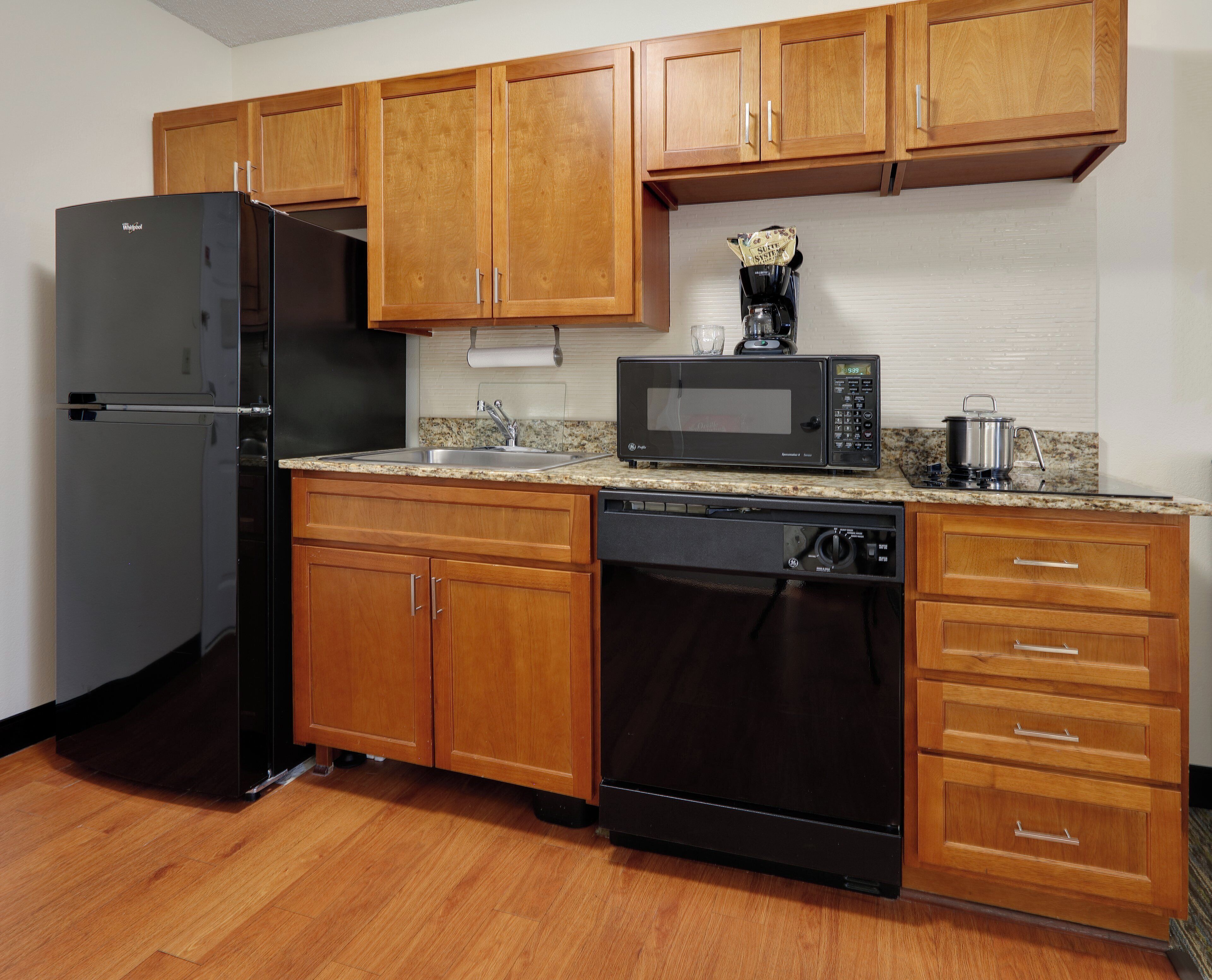 Una cocina con armarios de madera, un refrigerador negro, un microondas y un lavavajillas.