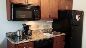 Una cocina con armarios de madera, un microondas de acero inoxidable, un refrigerador negro, una estufa y un lavavajillas.