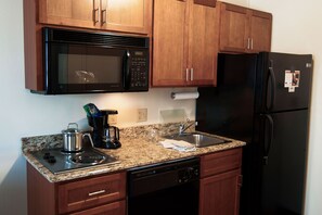 Una cocina con armarios de madera, un microondas de acero inoxidable, un refrigerador negro, una estufa y un lavavajillas.
