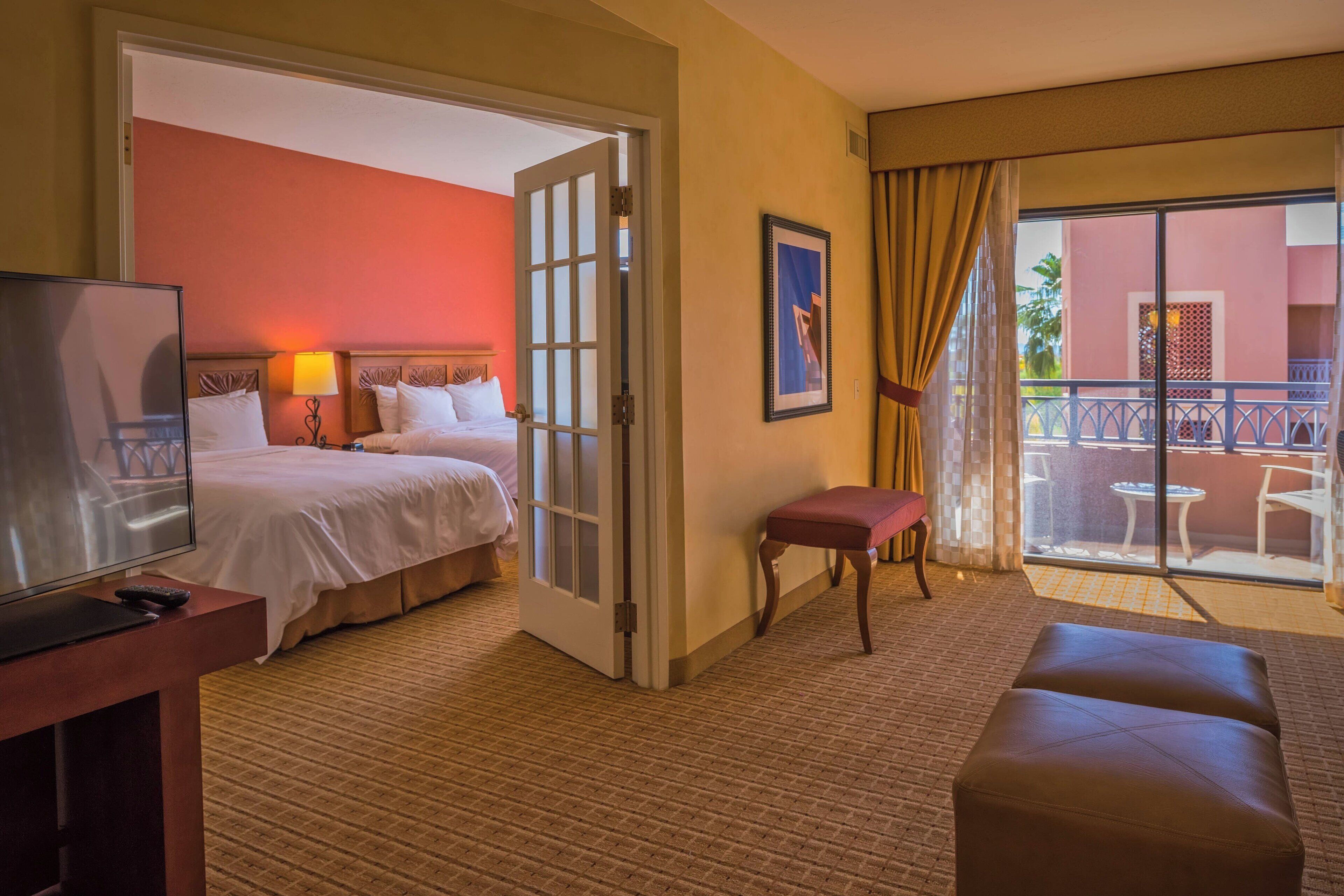 A hotel room with a bed, a TV, a desk, a chair, and a balcony with a table and chairs.