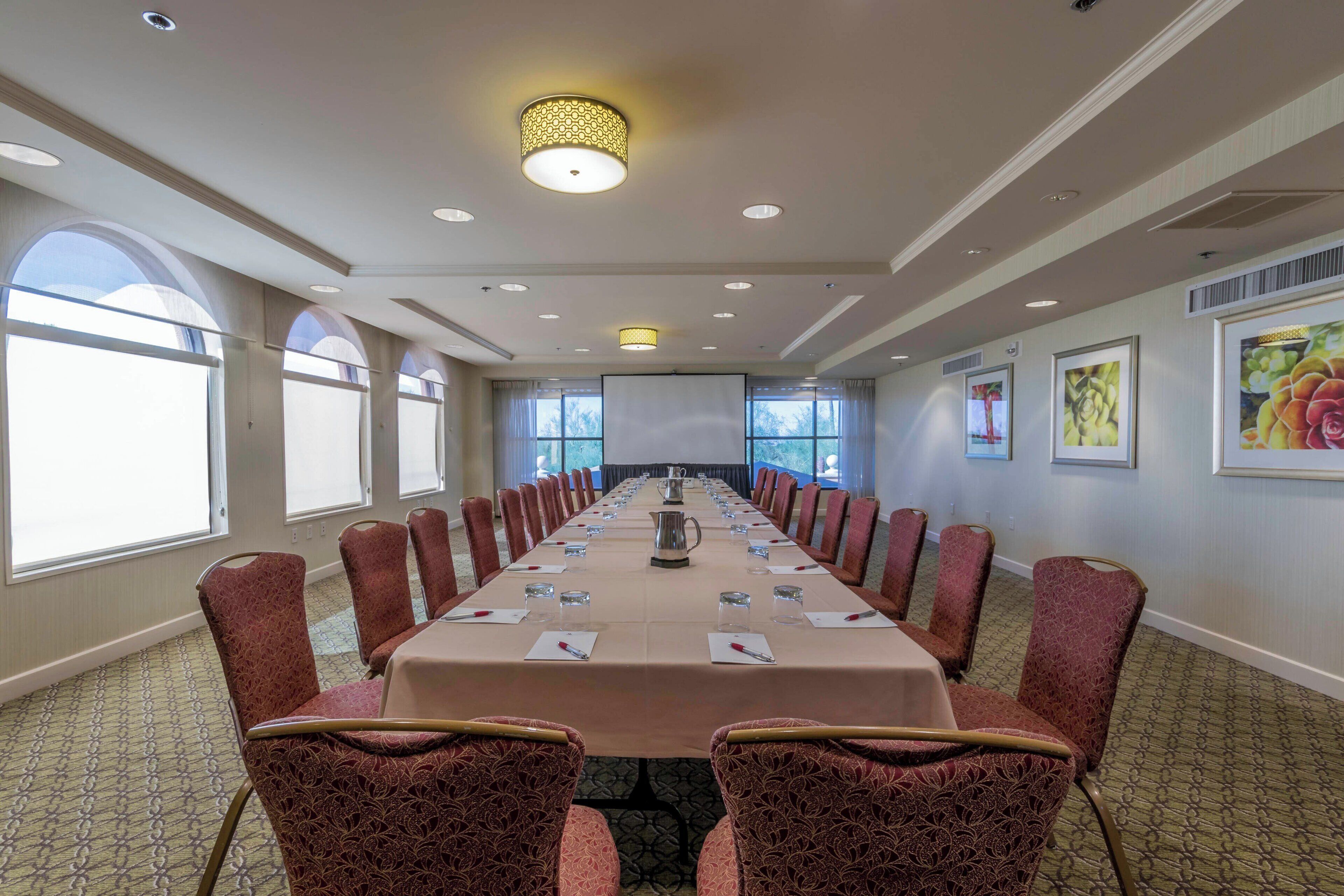 A conference room with a long table, red patterned chairs, and a projector screen at the front.