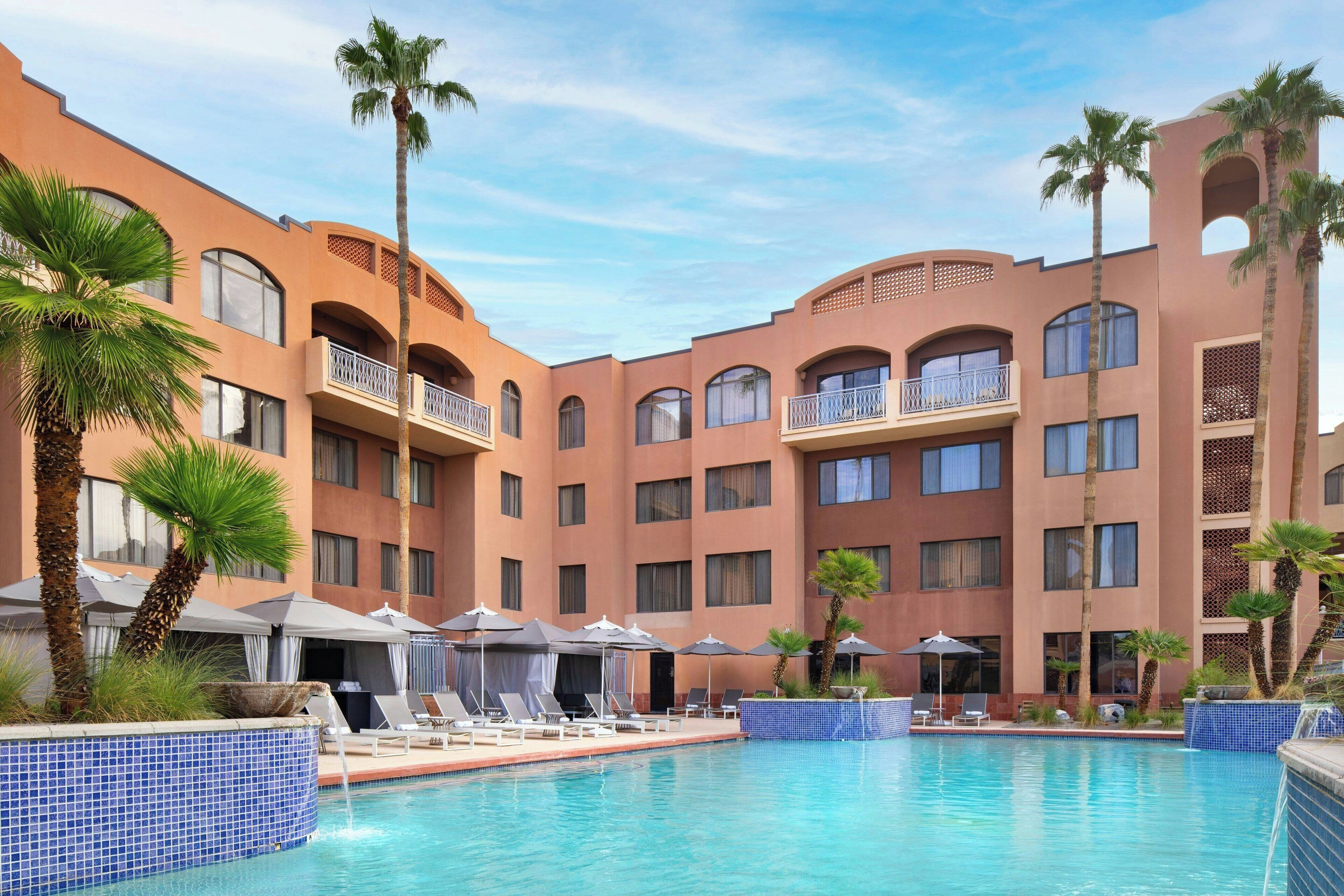 A hotel with a swimming pool, palm trees, and lounge chairs.