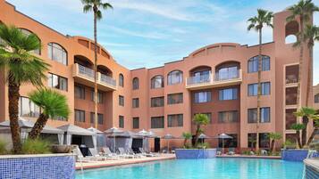 A hotel with a swimming pool, palm trees, and lounge chairs.