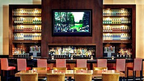 A bar area with multiple shelves of liquor bottles, a television screen, and a seating area with tables and chairs. - Scottsdale Marriott at McDowell Mountains (Scottsdale)
