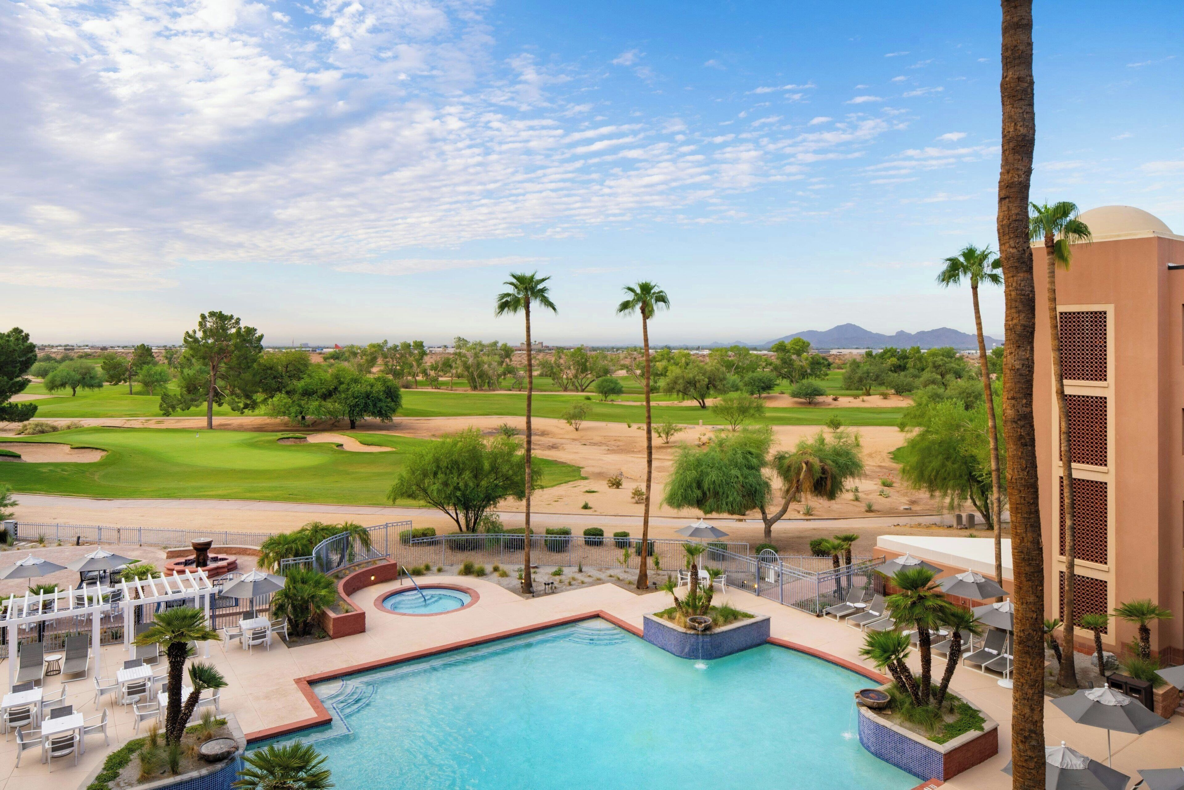 A pool area with a view of a golf course, palm trees, and a desert landscape.