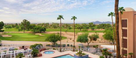 A pool area with a view of a golf course, palm trees, and a desert landscape.