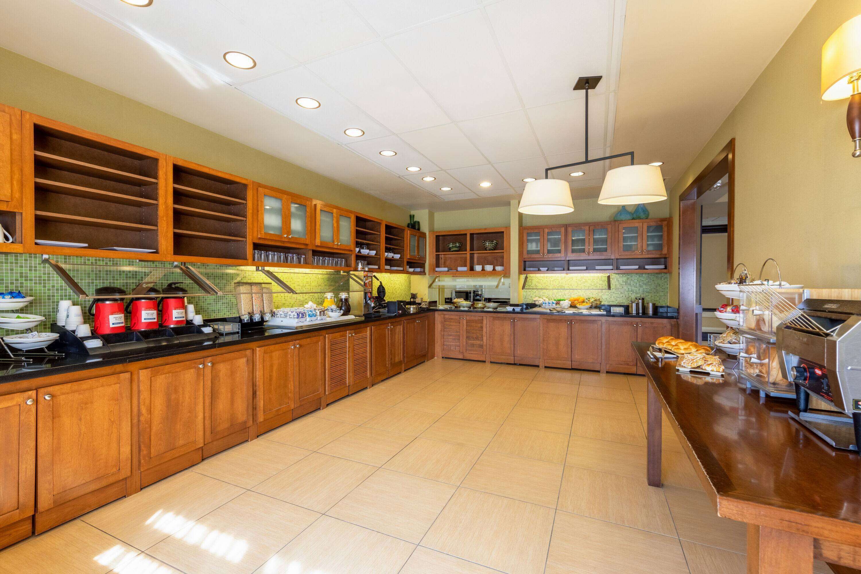 A spacious kitchen with wooden cabinets, a long counter, and a coffee station.