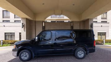 A black van parked under a covered area with a brick building in the background.