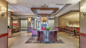 Un vestíbulo de hotel con una recepción central, zona de estar y un moderno candelabro.